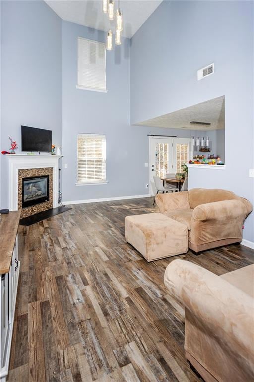 Living room featuring a towering ceiling, dark wood-style flooring, and a glass covered fireplace