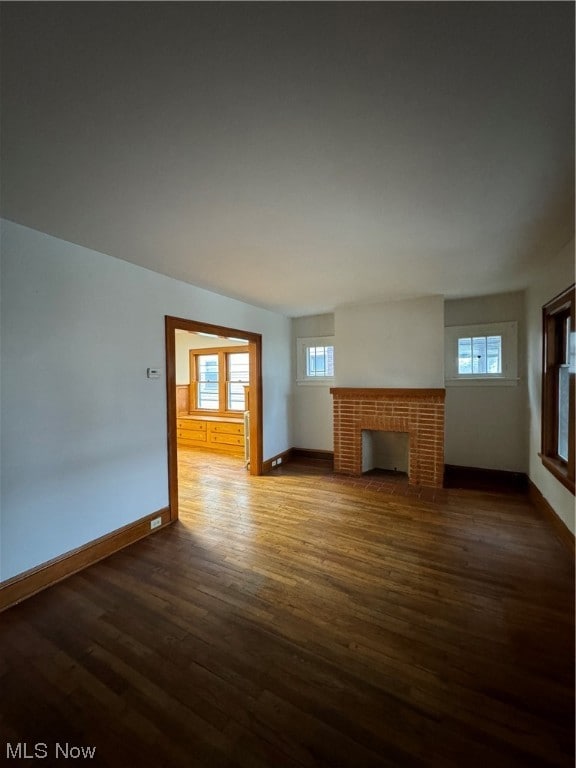 Unfurnished living room featuring a brick fireplace and dark hardwood / wood-style floors