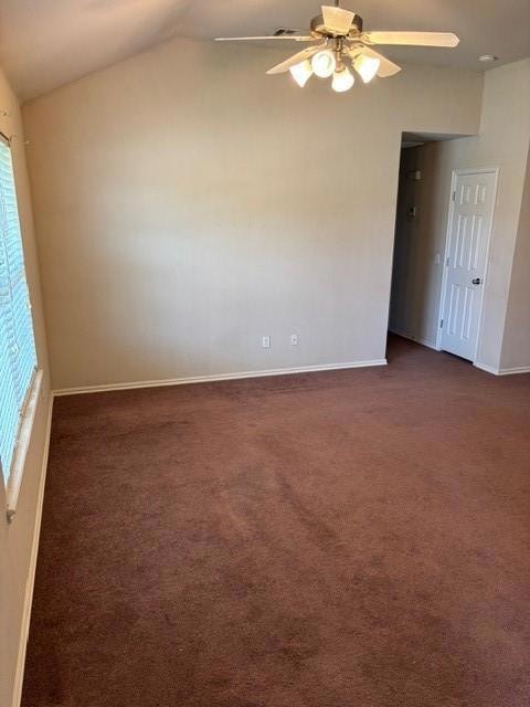 Unfurnished room featuring dark colored carpet, plenty of natural light, ceiling fan, and lofted ceiling