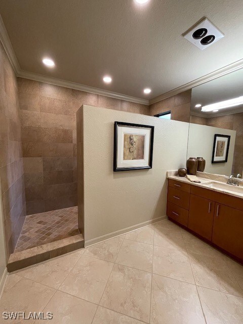 Bathroom featuring a tile shower, vanity, a textur