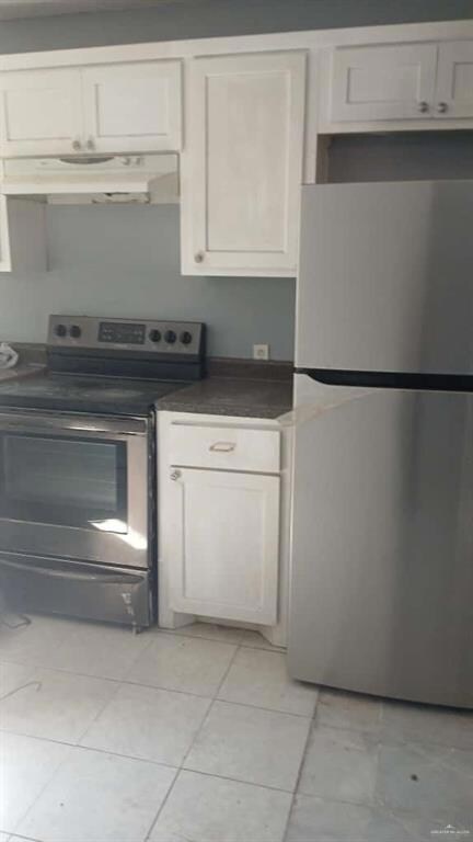 Kitchen with appliances with stainless steel finishes, under cabinet range hood, white cabinets, dark countertops, and light tile patterned floors