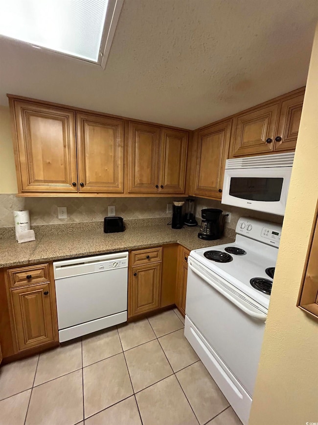 Kitchen featuring white appliances, light tile patterned floors, light stone countertops, and a textured ceiling