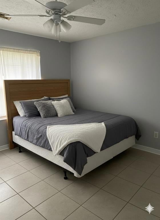 Bedroom with a textured ceiling, light tile. Patterned flooring, and ceiling fan.  Staged Photo.