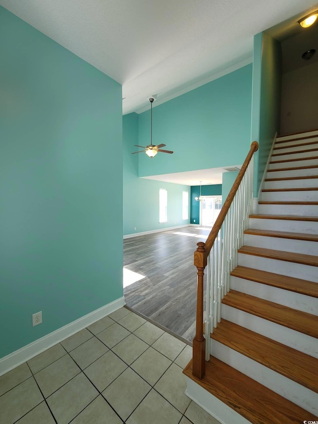 Staircase with ceiling fan, tile patterned floors, and lofted ceiling