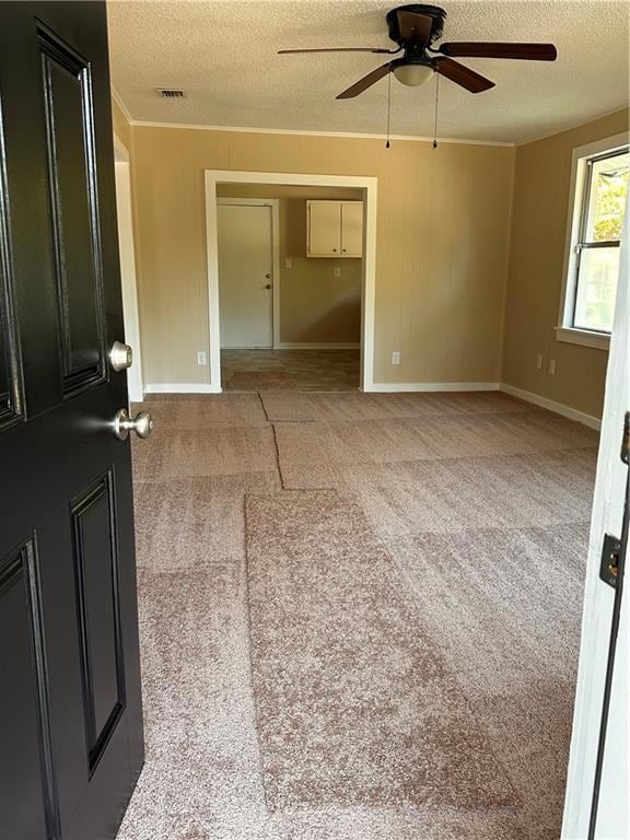Empty room with a textured ceiling, light colored carpet, a ceiling fan, and wooden walls