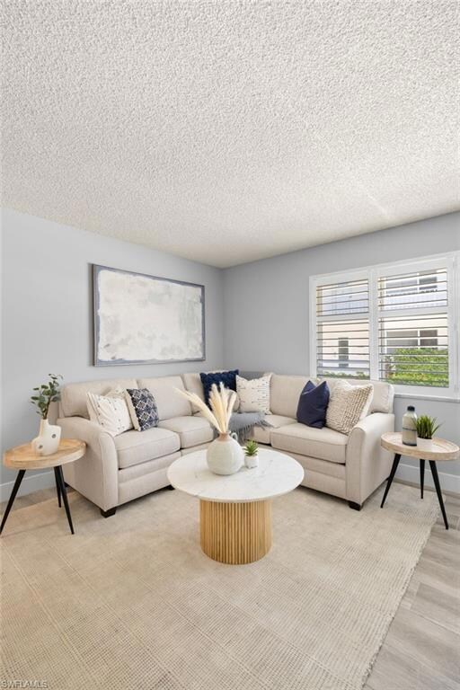 Living room with baseboards, a textured ceiling, and light wood finished floors