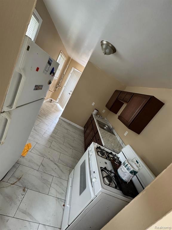 Kitchen featuring white appliances, dark brown cabinets, light countertops, and light marble finish flooring