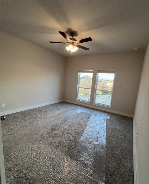 Carpeted spare room featuring a ceiling fan and ba
