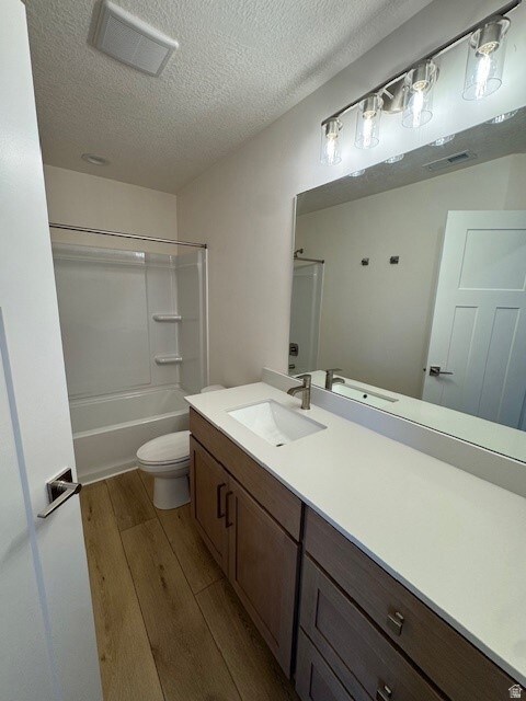 Bathroom featuring vanity, light wood finished floors, a textured ceiling, and tub / shower combination
