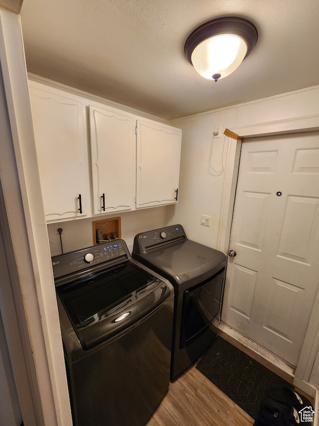 Washroom featuring light wood finished floors, cabinet space, and washer and clothes dryer