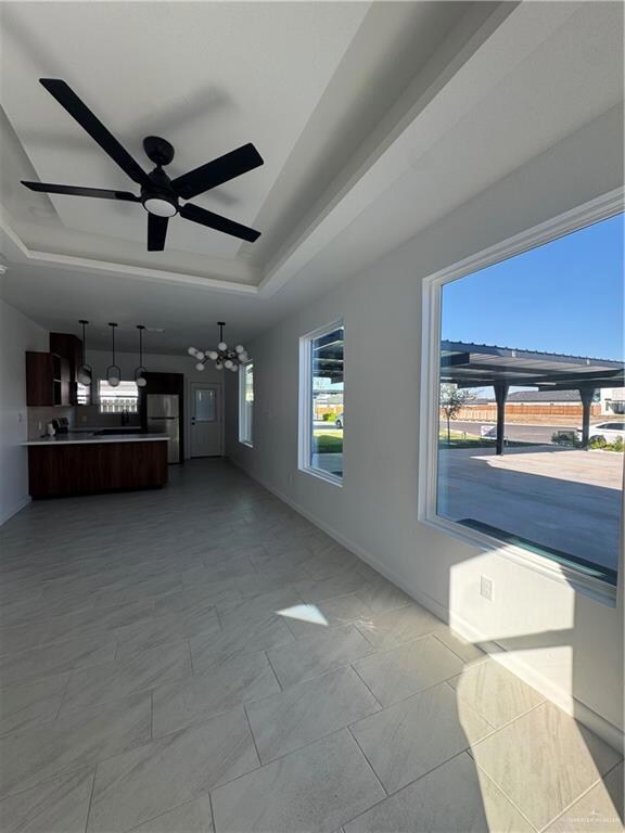 Unfurnished living room with a raised ceiling, a chandelier, and ceiling fan