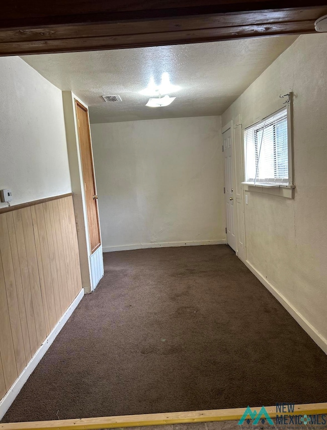 Spare room with dark carpet, a textured ceiling, and wooden walls