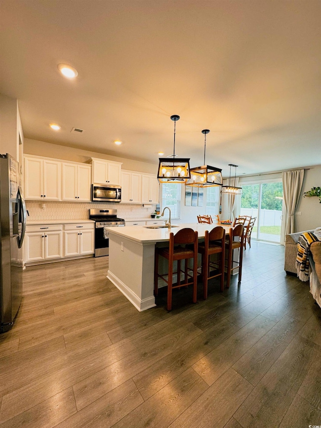 Kitchen featuring a kitchen bar, a center island with sink, decorative light fixtures, appliances with stainless steel finishes, and white cabinetry