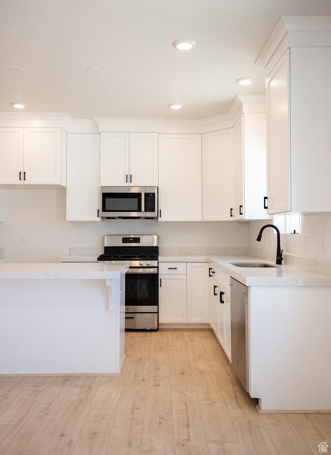 Kitchen with stainless steel appliances, white full height cabinetry, and light quartz countertops.