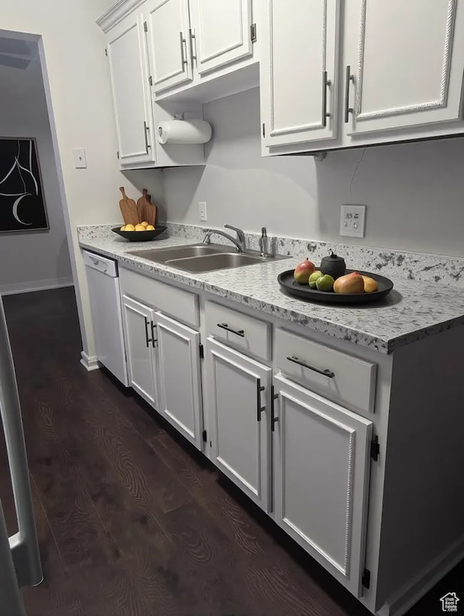 Kitchen featuring a sink, white dishwasher, light countertops, white cabinets, and dark wood-style floors