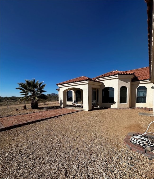 Back of house featuring a tile roof, a patio, and stucco siding