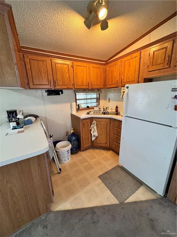 Kitchen featuring refrigerator, brown cabinets, light countertops, a textured ceiling, and lofted ceiling