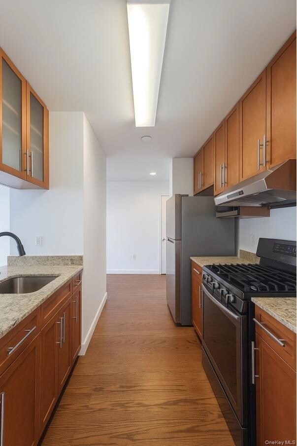 Kitchen with gas stove, light stone counters, light wood-type flooring, glass insert cabinets, and brown cabinets