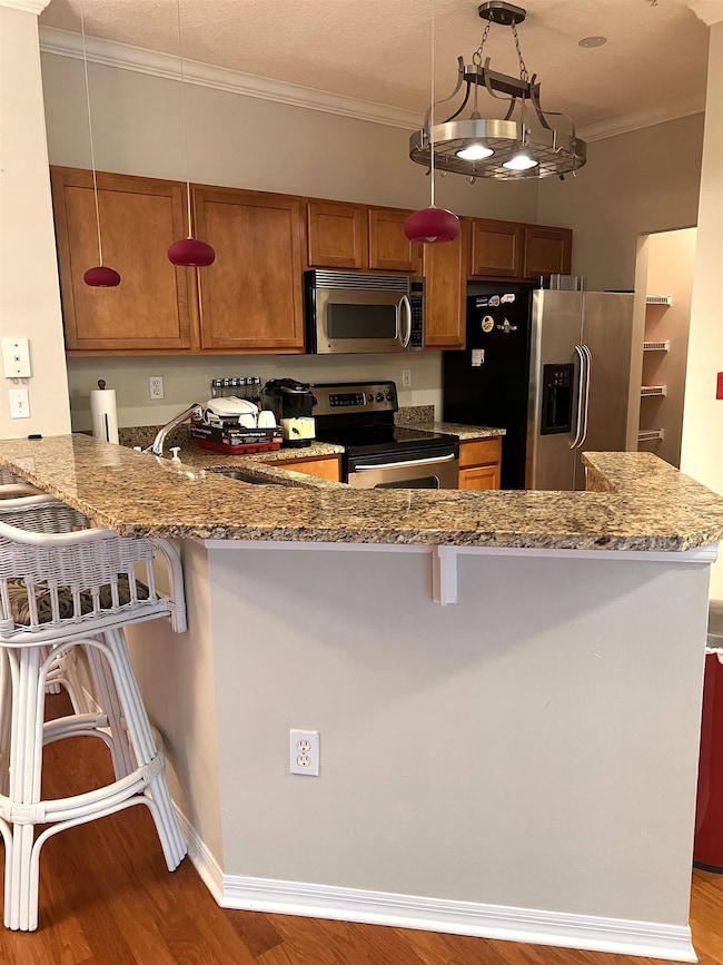 Kitchen featuring a breakfast bar, a peninsula, crown molding, dark stone countertops, and stainless steel appliances
