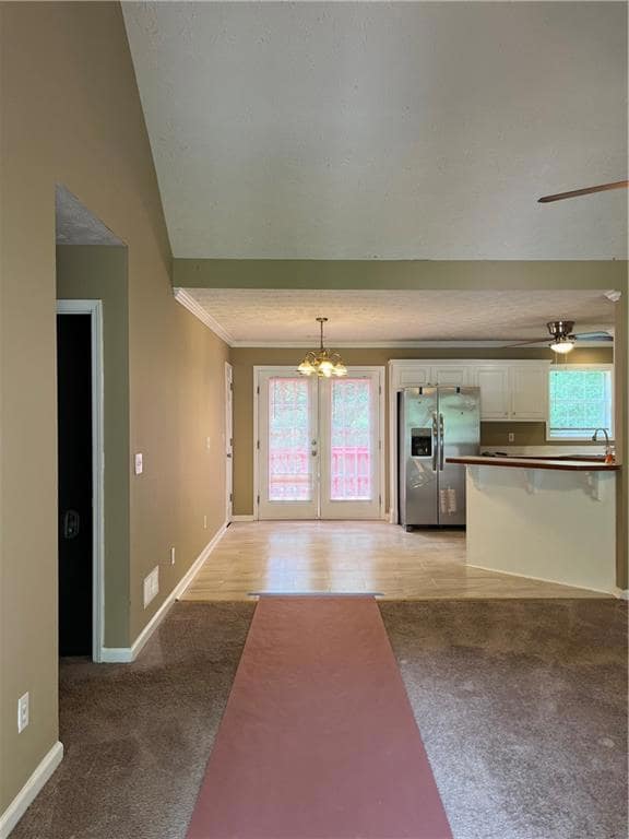 Unfurnished living room with light colored carpet, a chandelier, baseboards, crown molding, and french doors