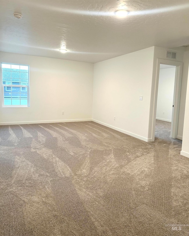 Carpeted spare room featuring a textured ceiling and baseboards