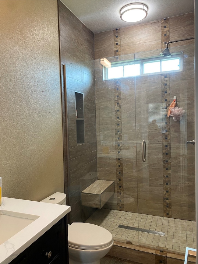 Full bath featuring a textured wall, vanity, a shower stall, and a textured ceiling