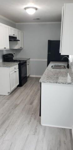 Kitchen featuring black / electric stove, light stone counters, white cabinetry, crown molding, and light wood-style floors