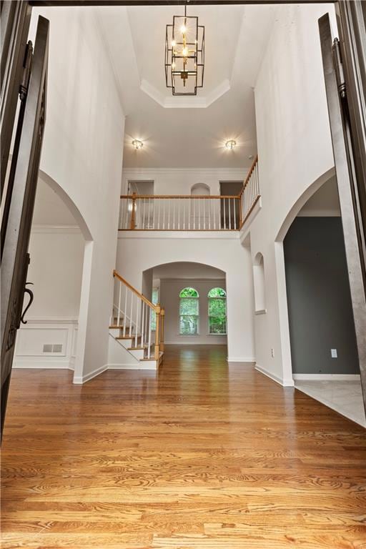 Foyer entrance with arched walkways, wood finished floors, stairway, a raised ceiling, and crown molding