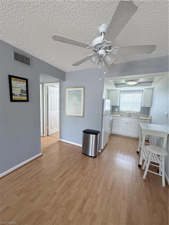Kitchen with fridge, light countertops, a textured ceiling, white cabinets, and light wood-type flooring