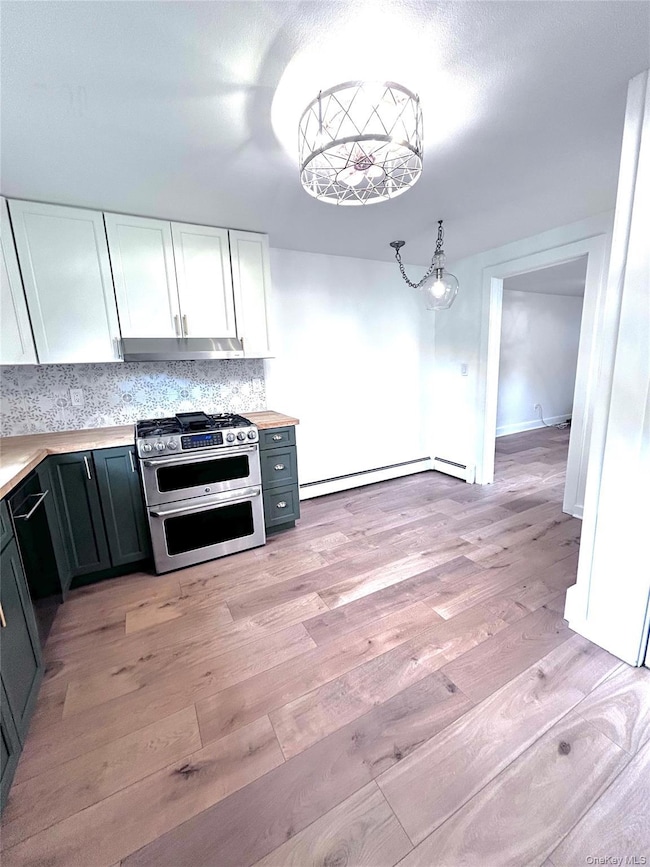Kitchen with double oven range, light countertops, white cabinets, decorative backsplash, and decorative light fixtures