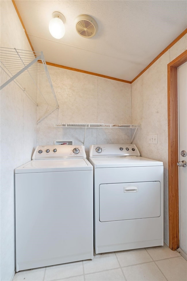 Washroom featuring ornamental molding, light tile patterned floors, and washing machine and clothes dryer