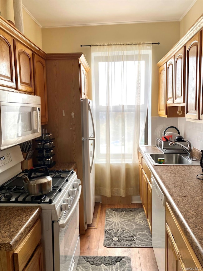 Kitchen with white appliances, dark countertops, tasteful backsplash, light wood-type flooring, and crown molding