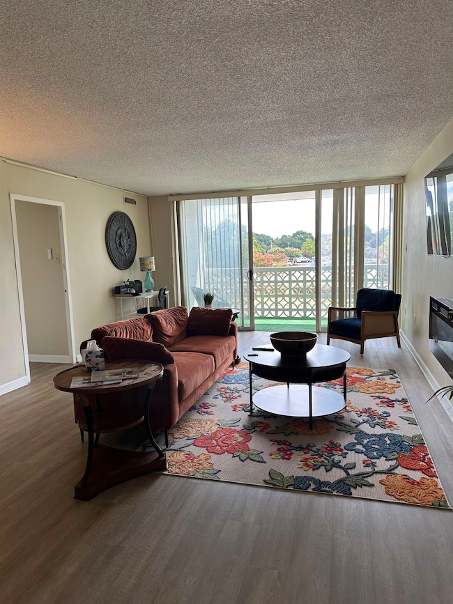 Living room with a wall of windows, wood finished floors, a textured ceiling, and a glass covered fireplace