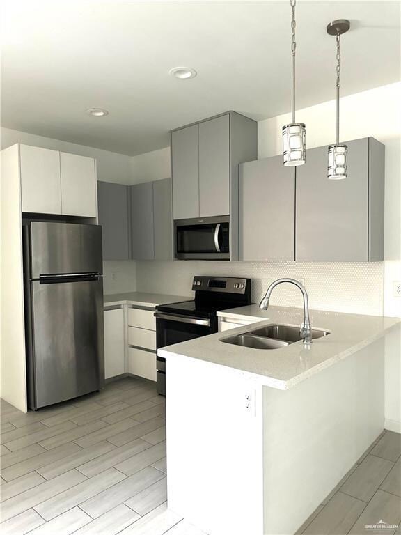 Kitchen featuring appliances with stainless steel finishes, a peninsula, decorative light fixtures, gray cabinetry, and recessed lighting