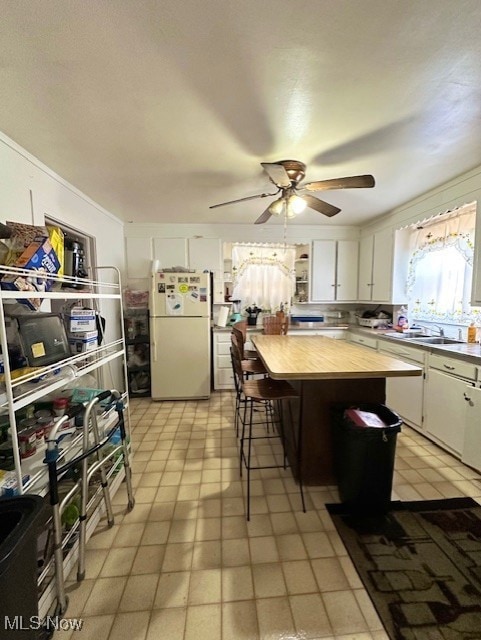 Kitchen featuring white cabinets, freestanding refrigerator, crown molding, a breakfast bar area, and a kitchen island