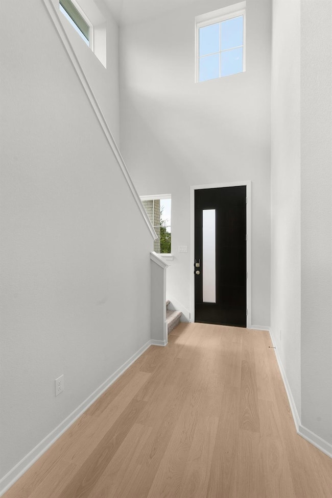 Foyer with light wood-type flooring, a towering ceiling, and stairs