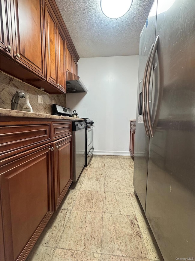 Kitchen with stainless steel appliances, a textured ceiling, backsplash, light stone countertops, and exhaust hood