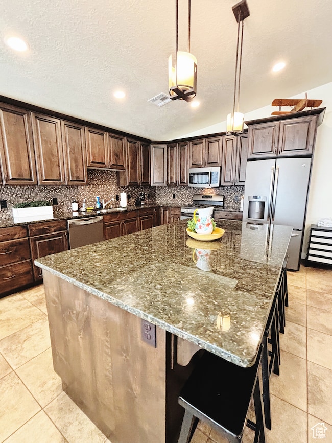 Kitchen with stainless steel appliances, decorative backsplash, dark stone counters, a spacious island, and lofted ceiling