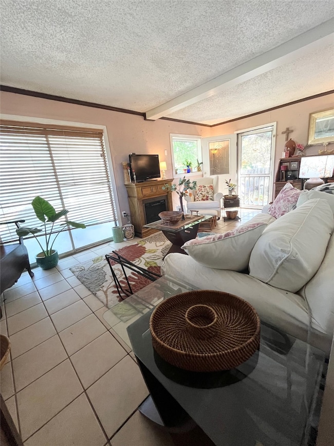 Living area featuring tile patterned floors, a textured ceiling, a fireplace, beam ceiling, and ornamental molding