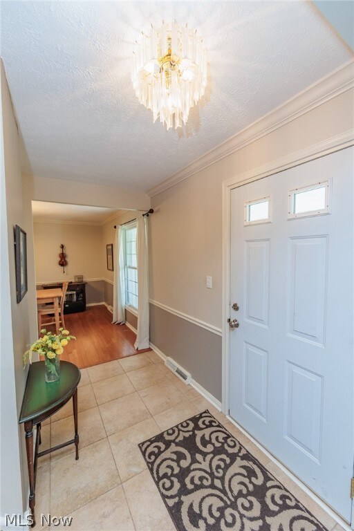 Tiled entrance foyer featuring ornamental molding, a textured ceiling, and a notable chandelier