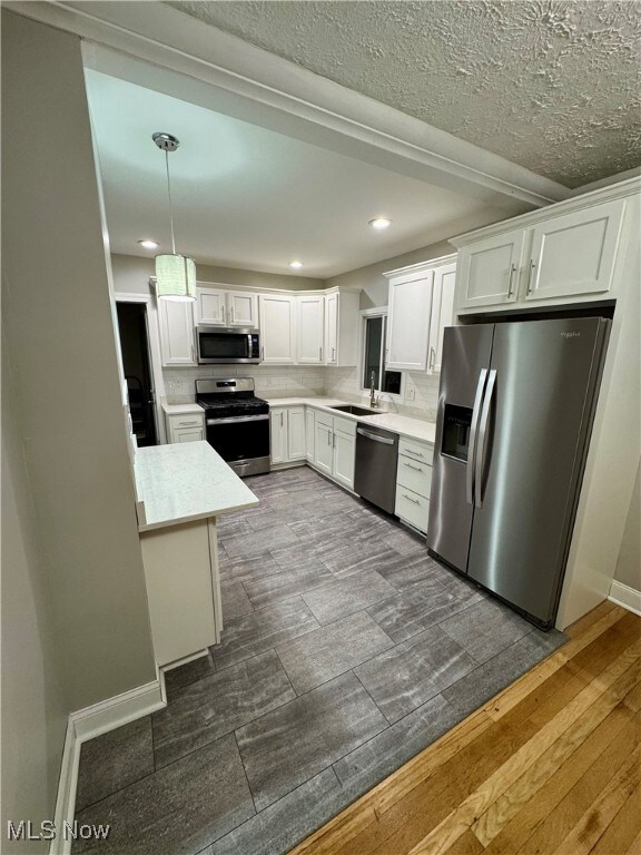 Kitchen with appliances with stainless steel finishes, hanging light fixtures, white cabinetry, dark hardwood / wood-style floors, and sink