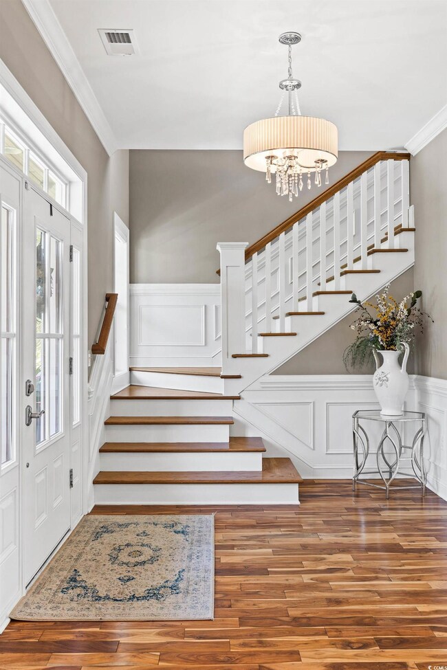 Entrance foyer with stairway, a chandelier, ornamental molding, wood finished floors, and a decorative wall