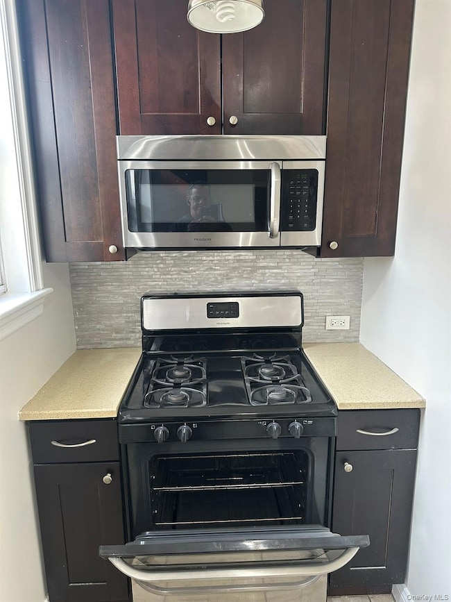 Kitchen featuring gas range oven, stainless steel microwave, tasteful backsplash, dark brown cabinetry, and light stone counters