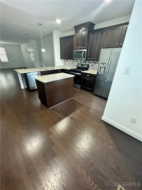 Kitchen featuring pendant lighting, a center island, appliances with stainless steel finishes, dark hardwood / wood-style flooring, and light stone countertops