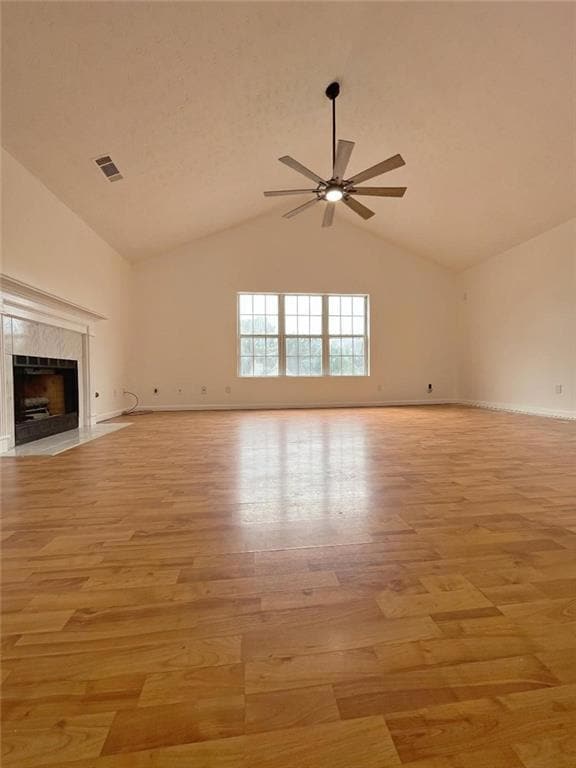Unfurnished living room featuring light wood-style floors, a ceiling fan, vaulted ceiling, a high end fireplace, and baseboards