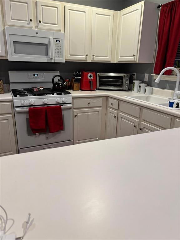 Kitchen featuring white appliances, light countertops, and white cabinetry