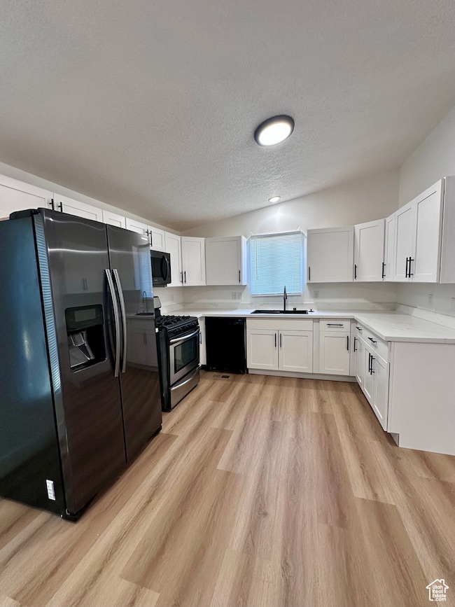 Kitchen with black appliances, a textured ceiling, light countertops, white cabinets, and light wood-style flooring
