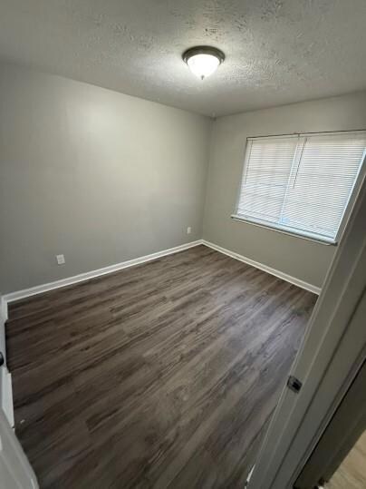 Unfurnished room featuring baseboards, wood finished floors, and a textured ceiling