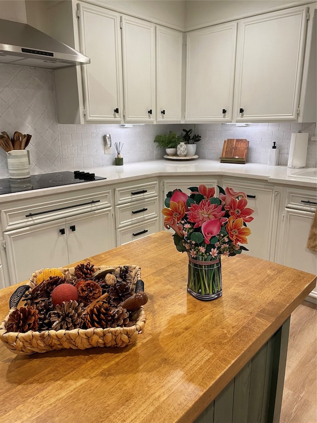 Kitchen featuring white cabinets, exhaust hood, decorative backsplash, stovetop, and wooden counters