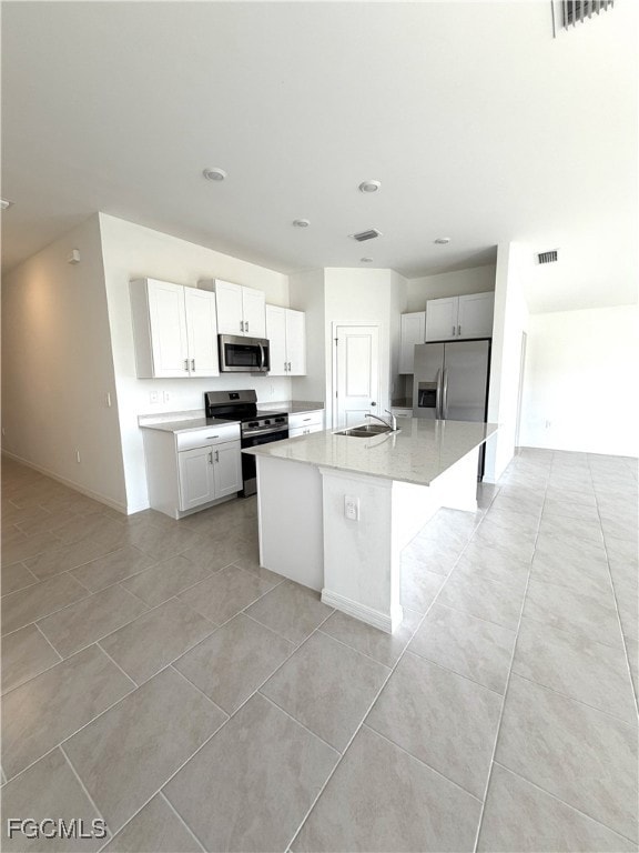 Kitchen featuring stainless steel appliances, an island with sink, light tile patterned floors, light stone countertops, and recessed lighting